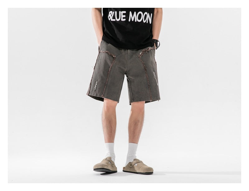 Person wearing dark gray frayed-seam shorts with a black graphic tee, white socks and tan clogs, front view