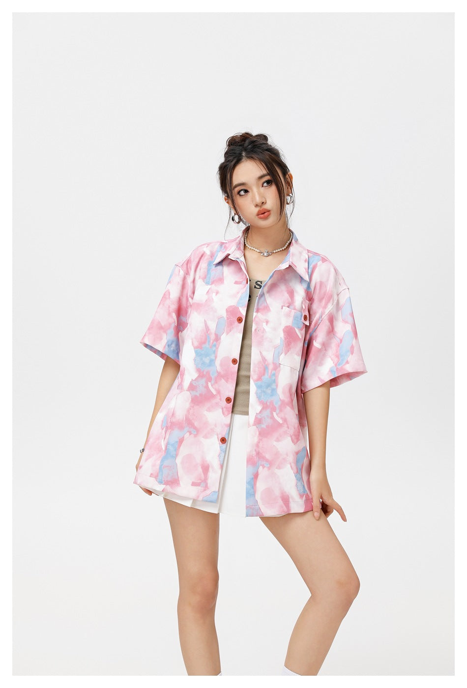 Model wearing an oversized pink and blue abstract-print button-up shirt over a white top and skirt.