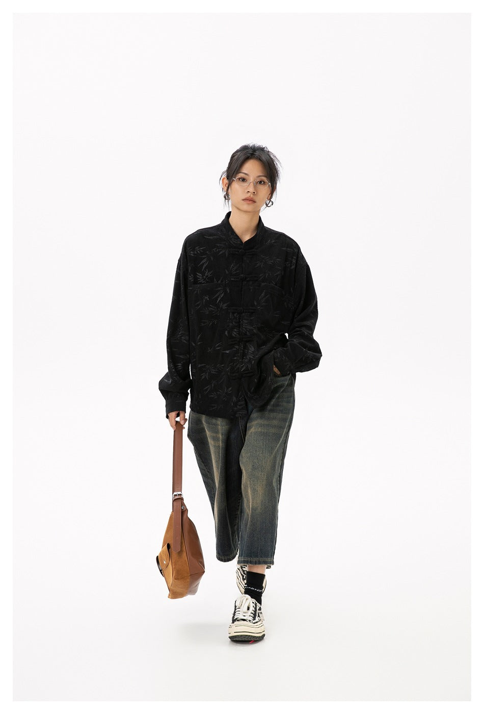 Woman walking in black bamboo-pattern frog-knot shirt with faded jeans and holding a tan shoulder bag
