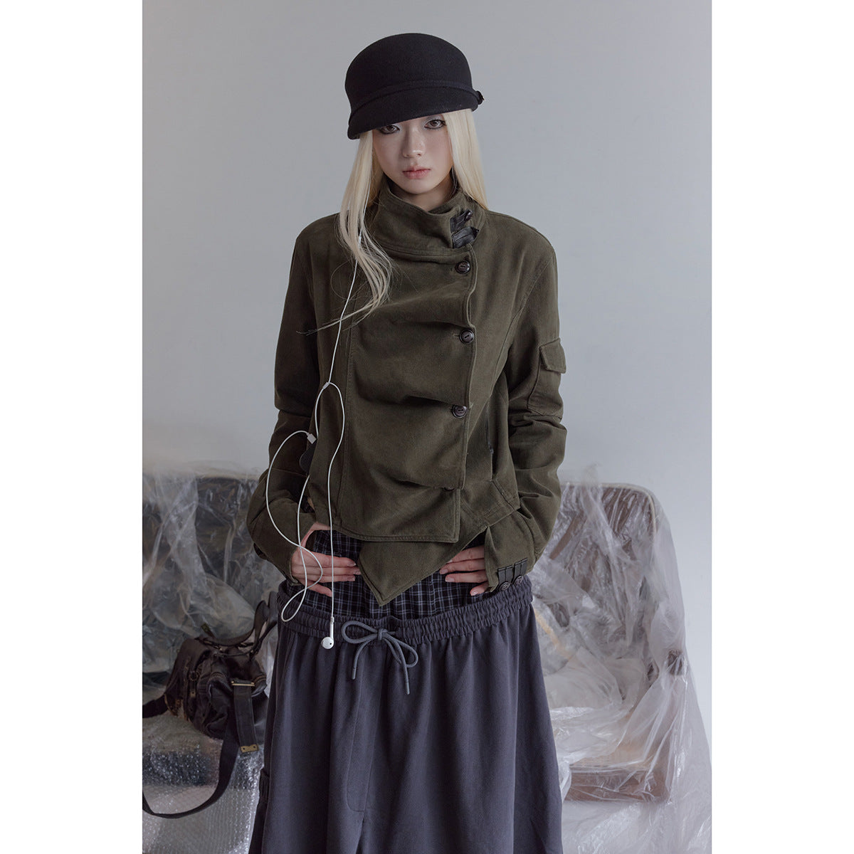 Model wearing an olive asymmetrical jacket with a high collar and dark buttons, paired with a long charcoal skirt.