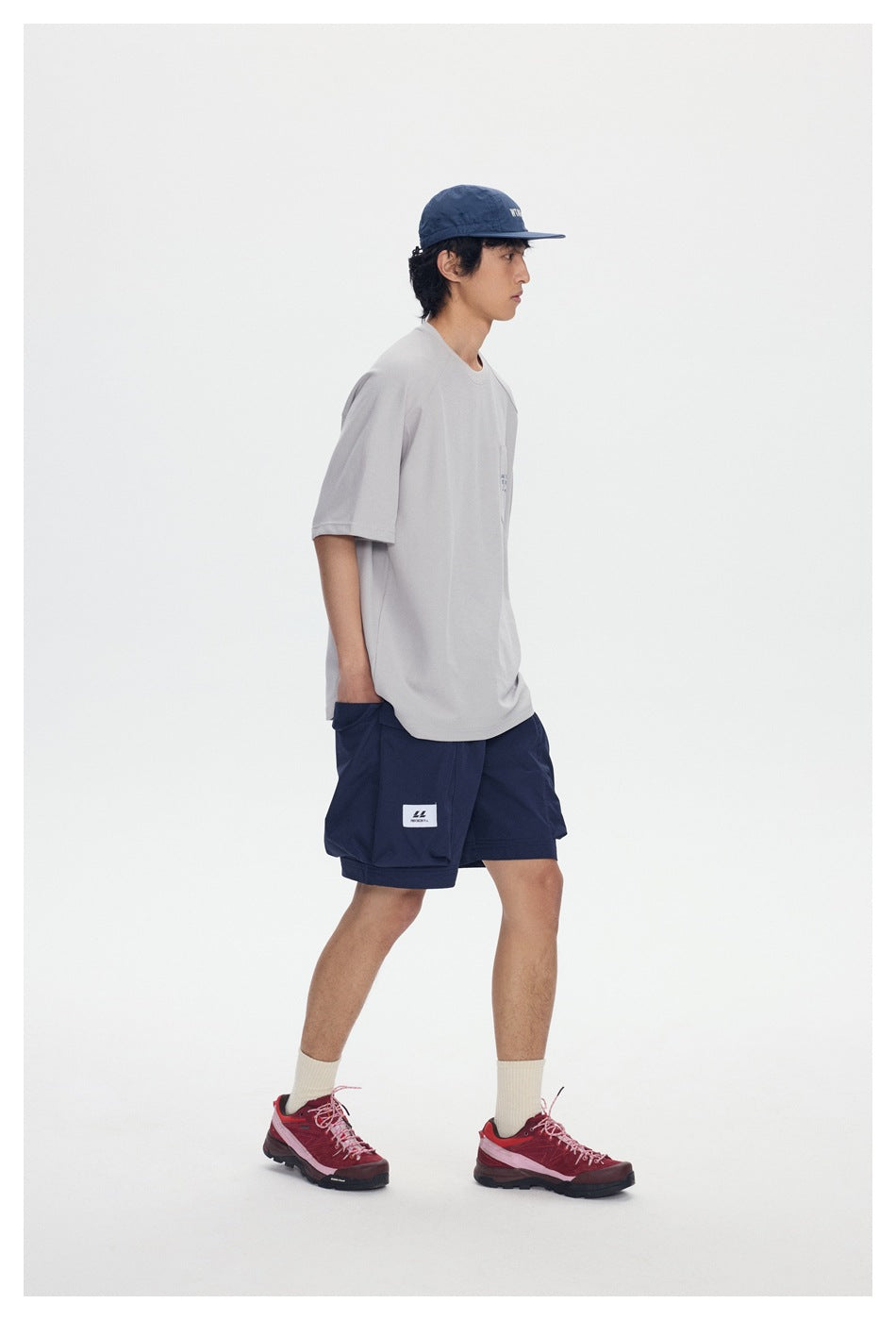Side view of a model wearing a light gray pocket T-shirt, navy cargo shorts, and a navy cap.