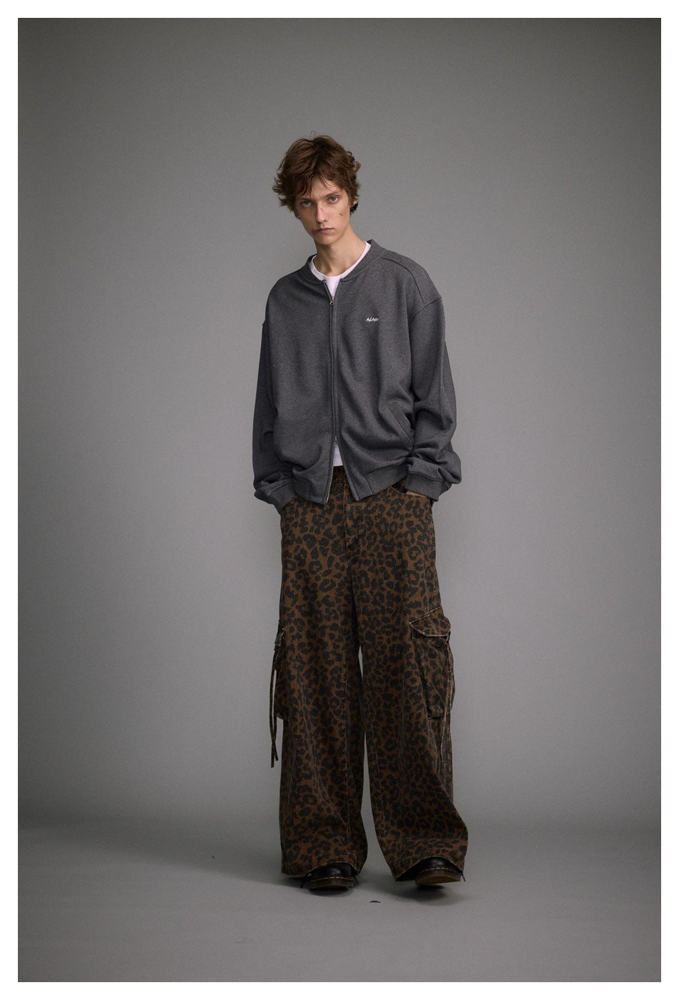 Model wearing a charcoal gray zip-front jacket and brown leopard-print cargo pants, shown nearly full length.