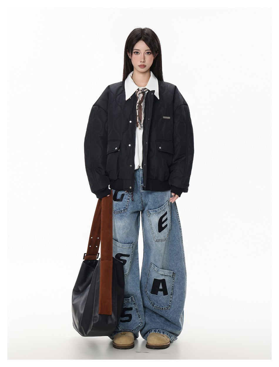Full-length model wearing a black quilted bomber jacket with flap pockets, styled with loose lettered jeans and a tote.