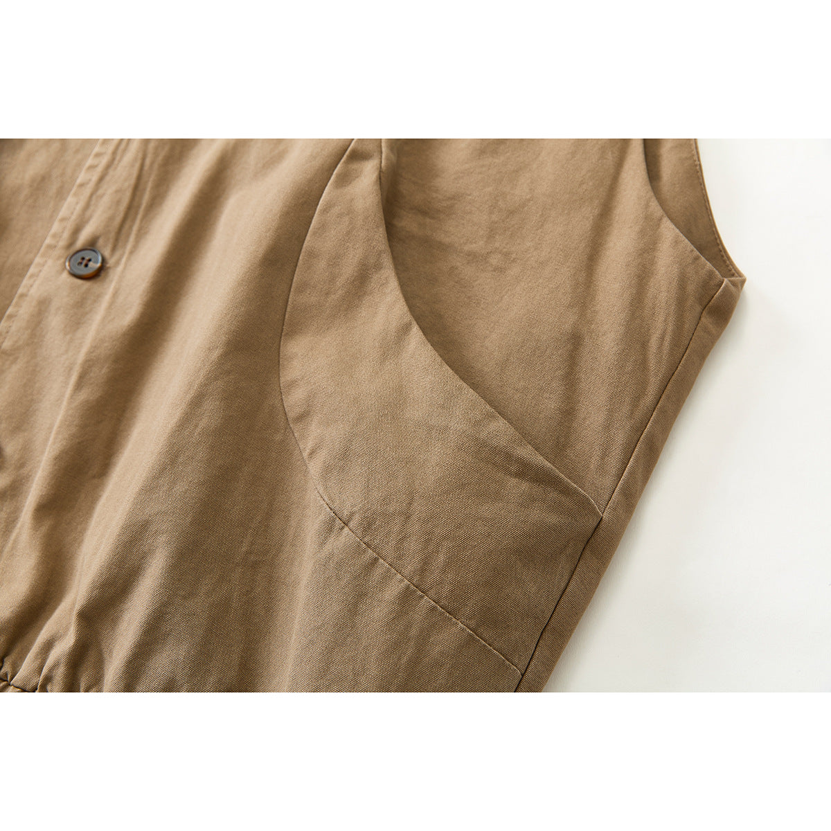 Close-up of the tan vest's side seam, armhole, and a dark button.