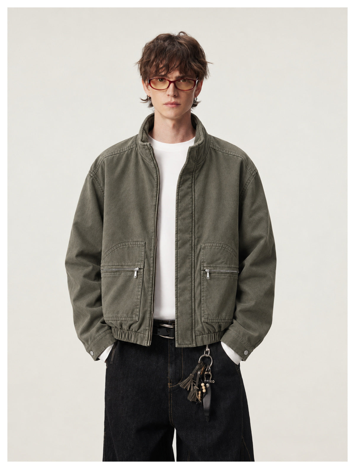 Close-up of model in army green stand-collar jacket with zip pockets over a white tee and dark jeans