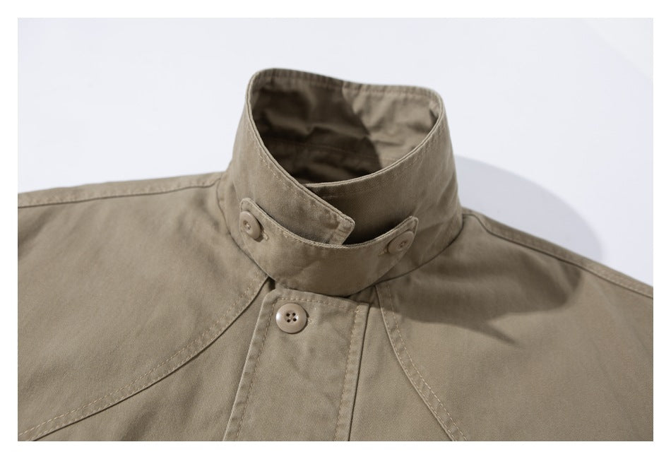 Close-up of a taupe jacket's tall stand collar with overlapping buttoned tabs and stitched shoulder seams.