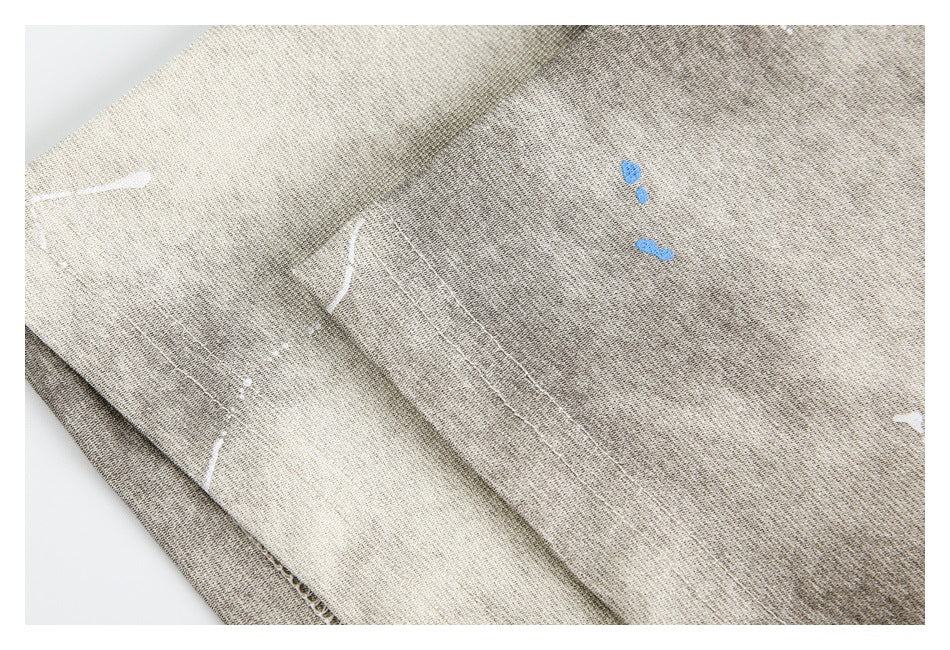Close-up of overlapping gray-beige garment panels with stitching and scattered white and blue marks.