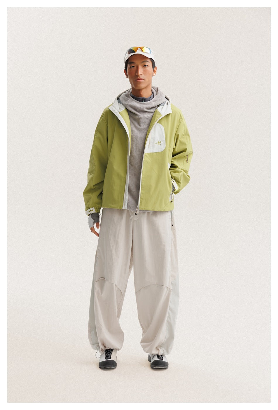 Model wears a lime green hooded jacket with a white chest pocket, gray top, and loose off-white pants.