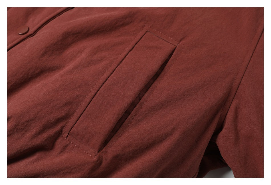 Close-up of a slanted welt pocket on rust-red garment fabric.