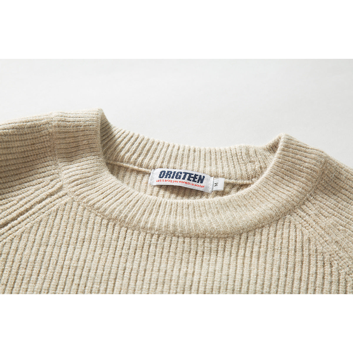 Close-up of a cream rib-knit sweater's crew neckline and sewn neck label.