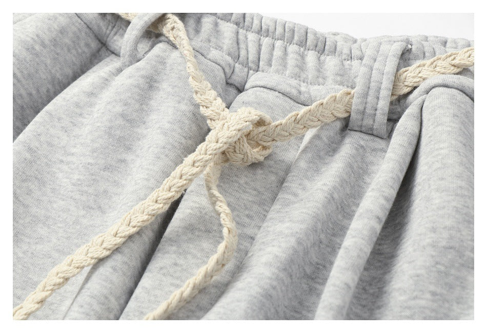 Close-up of light gray heathered sweatpants with an elastic waistband and cream braided drawstring.