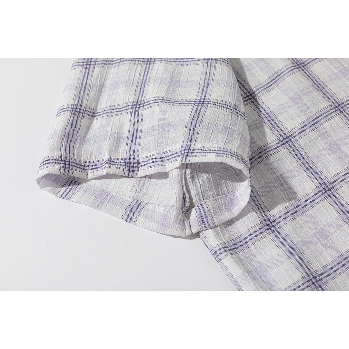 Close-up of the short sleeve and hem of a pale lavender and white plaid shirt.