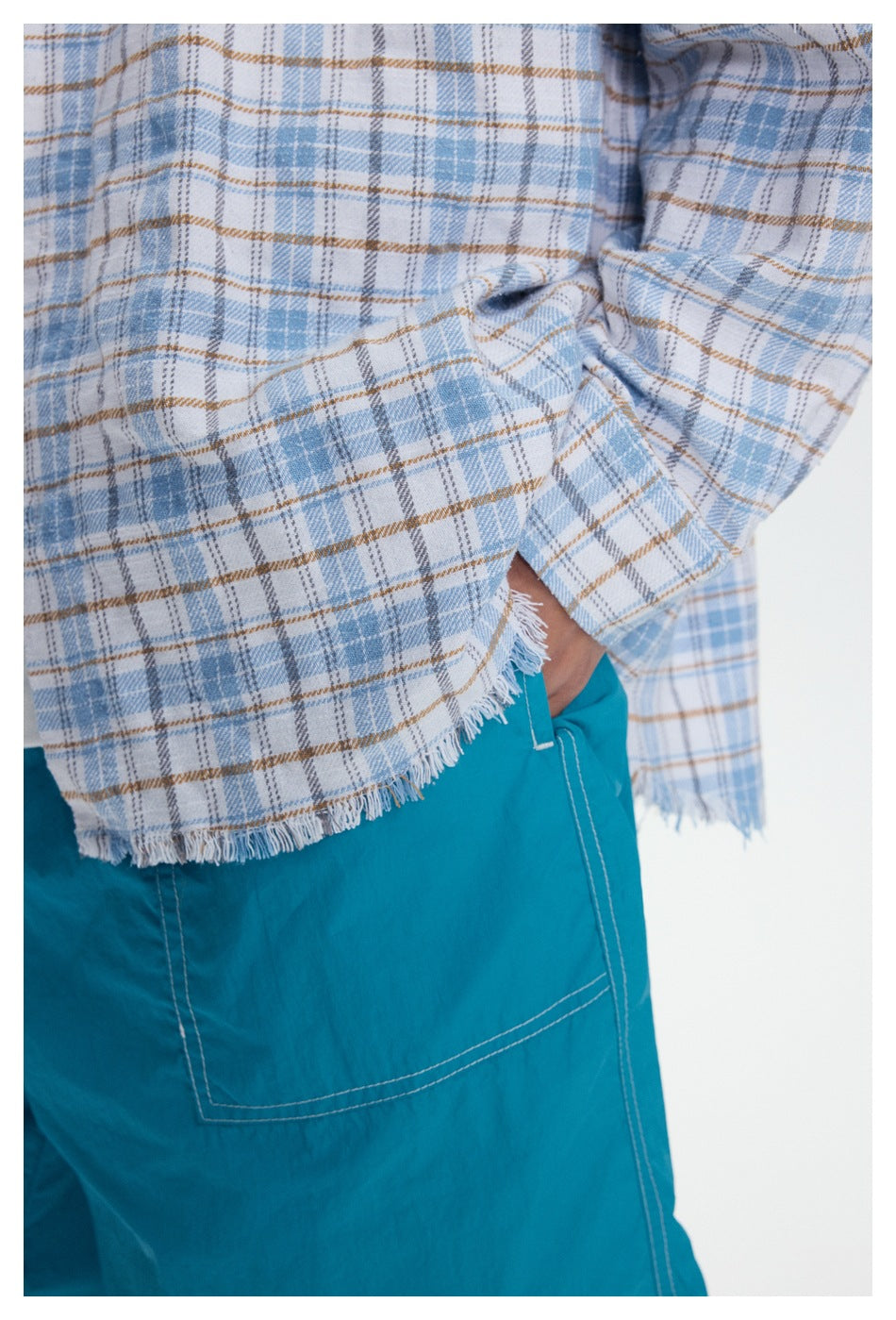 Close-up of the plaid shirt's frayed hem beside turquoise shorts with a stitched pocket.