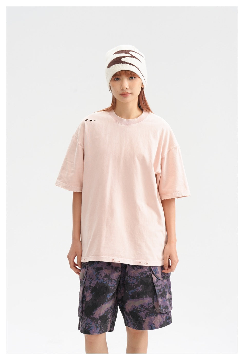 Closer view of a model wearing an oversized pale pink T-shirt and purple camouflage cargo shorts.