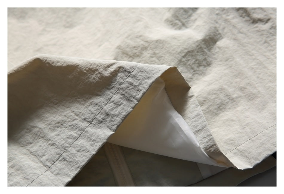 Close-up of a light beige garment with the hem lifted to show its white inner lining and stitched seams.
