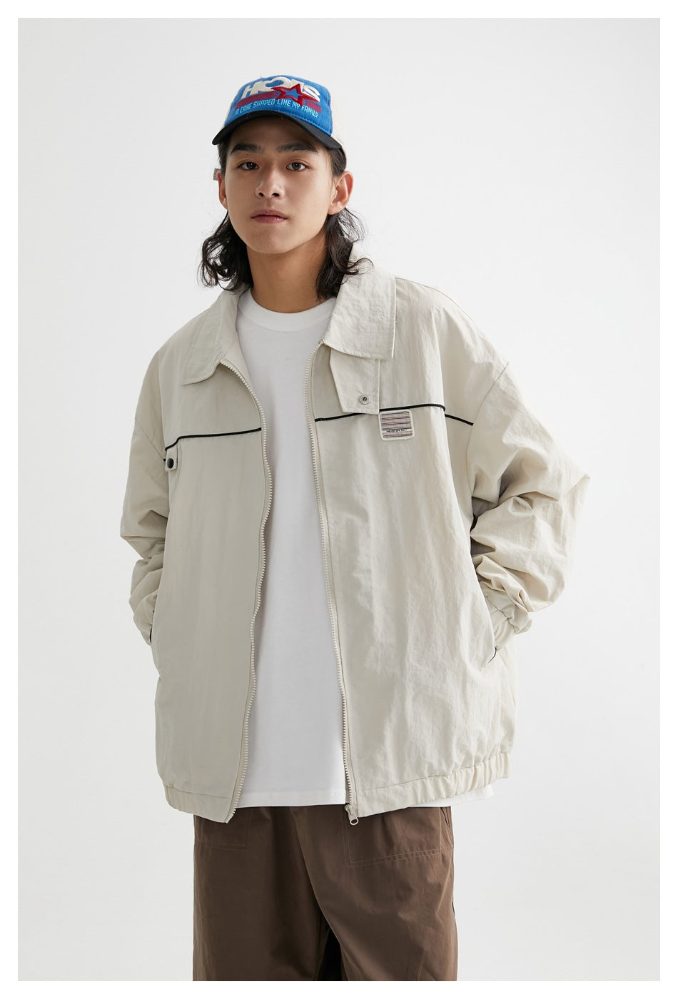 Model wearing an open ivory zip jacket with black piping, a chest patch, and an elastic hem.