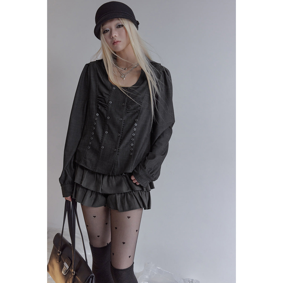 Model wearing a charcoal long-sleeve button-front blouse and layered ruffle mini skirt with heart-print tights.