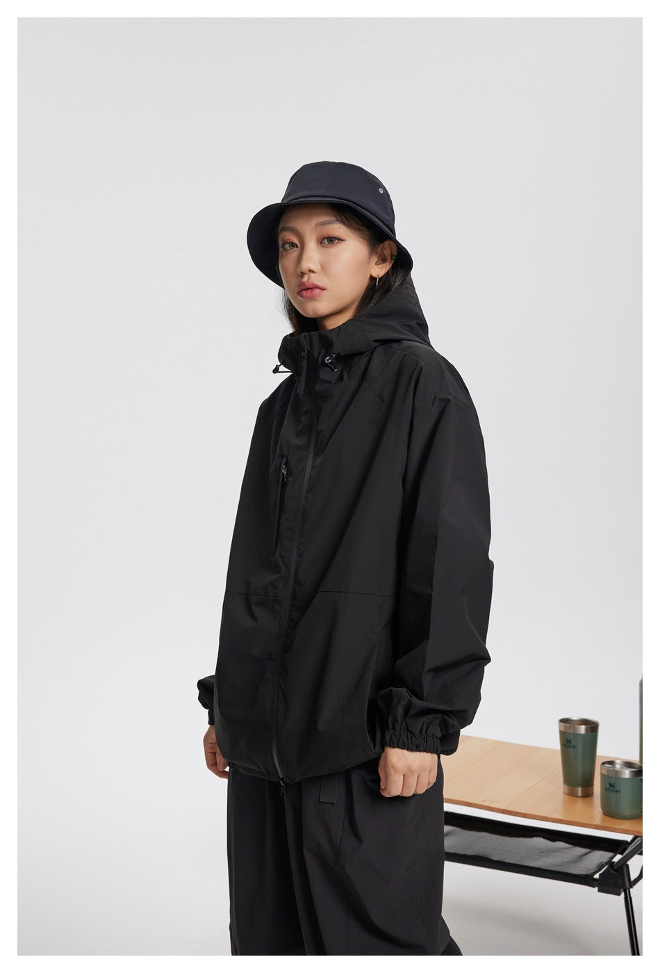 Three-quarter view of a woman wearing a black hooded jacket with elastic cuffs and a front zipper.