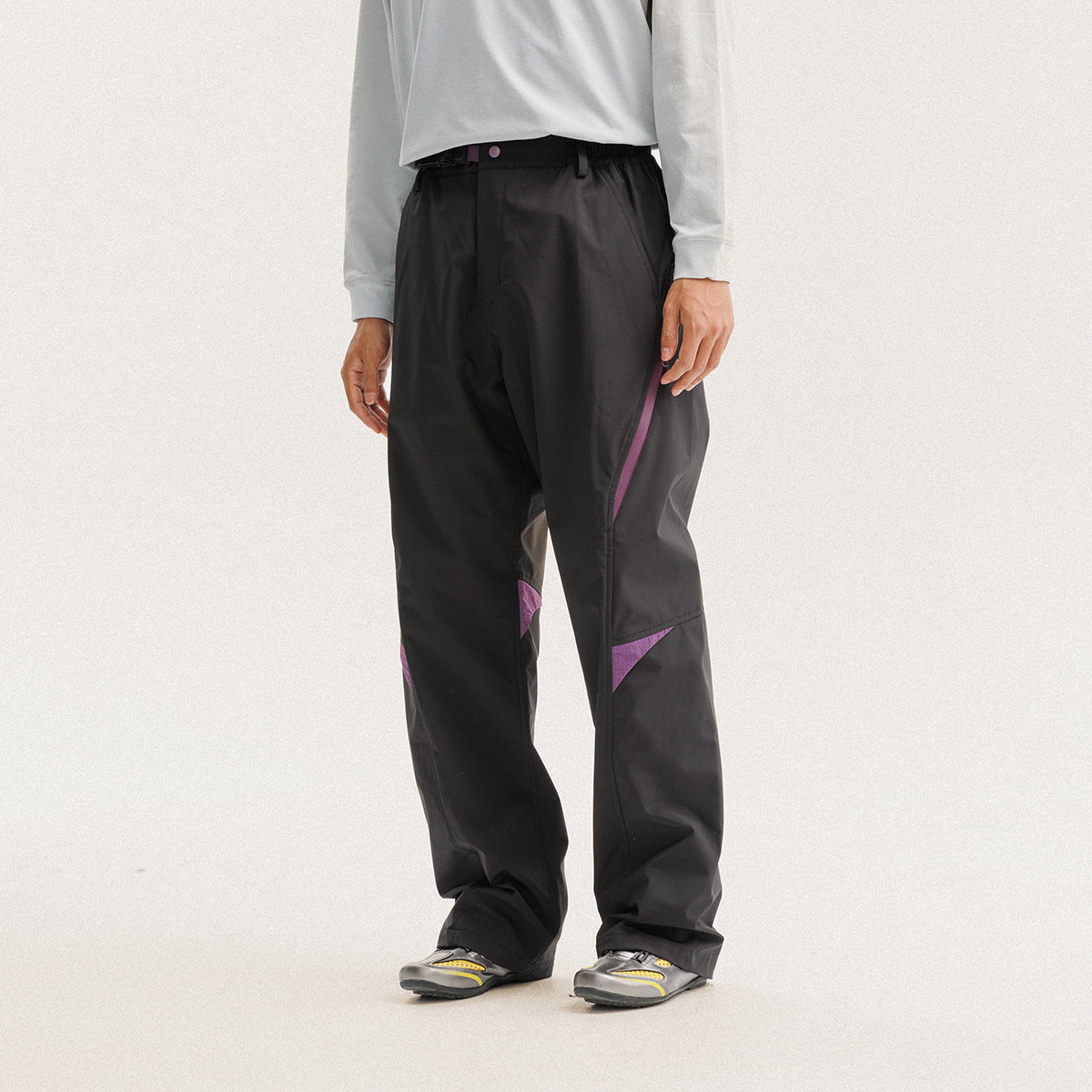 Model wearing loose black trousers with an elastic waist and purple diagonal zip and knee accents.