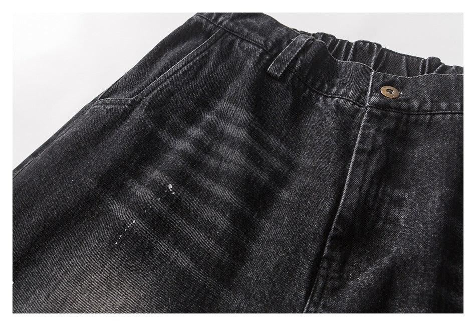 Close-up of black washed trousers showing the buttoned waistband, belt loop, and white paint flecks.
