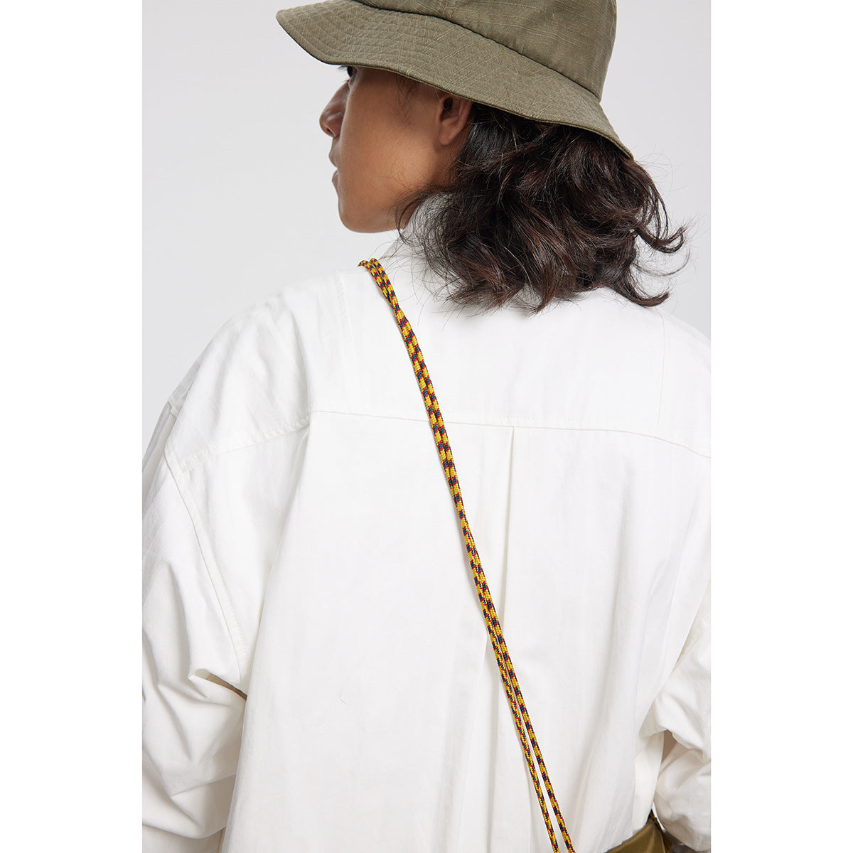 Rear close-up of a model in a white shirt, with a colorful cord crossing the back.