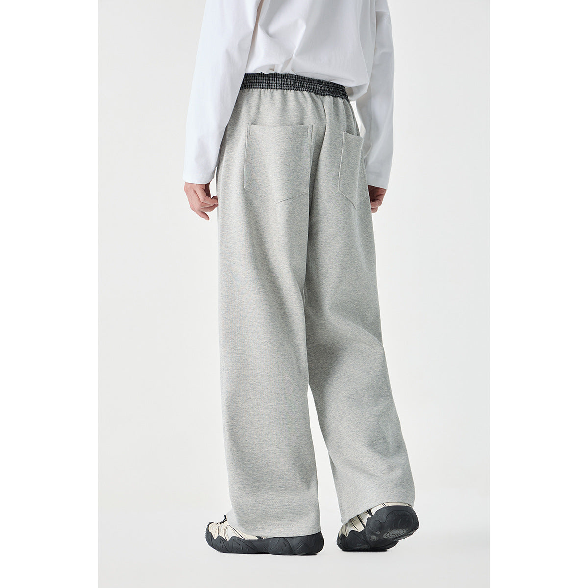 Back view of a model wearing light gray wide-leg pants with a checked waistband and two rear patch pockets.