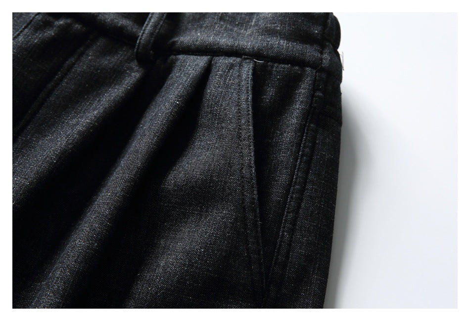Close-up of black textured trousers showing the gathered waistband and stitched pleated side seam.