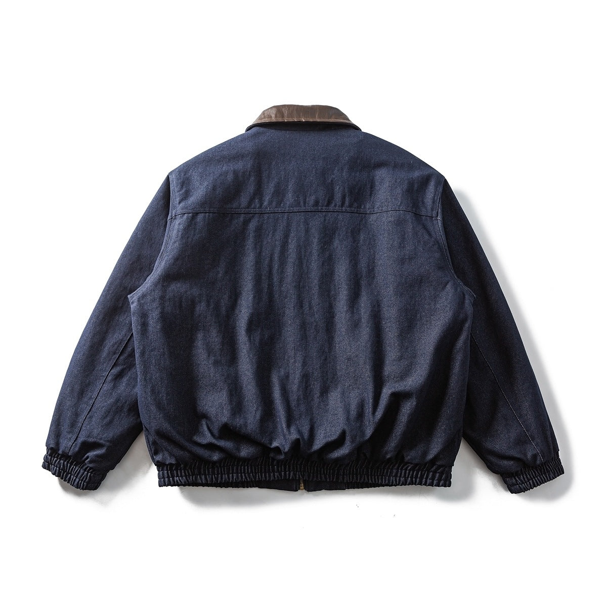 Back view of a dark indigo jacket with a brown collar and gathered cuffs and hem, laid flat.