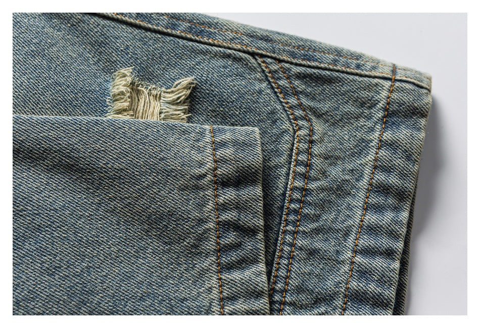 Close-up of washed blue denim showing a frayed distressed patch beside stitched seams and a pocket edge.