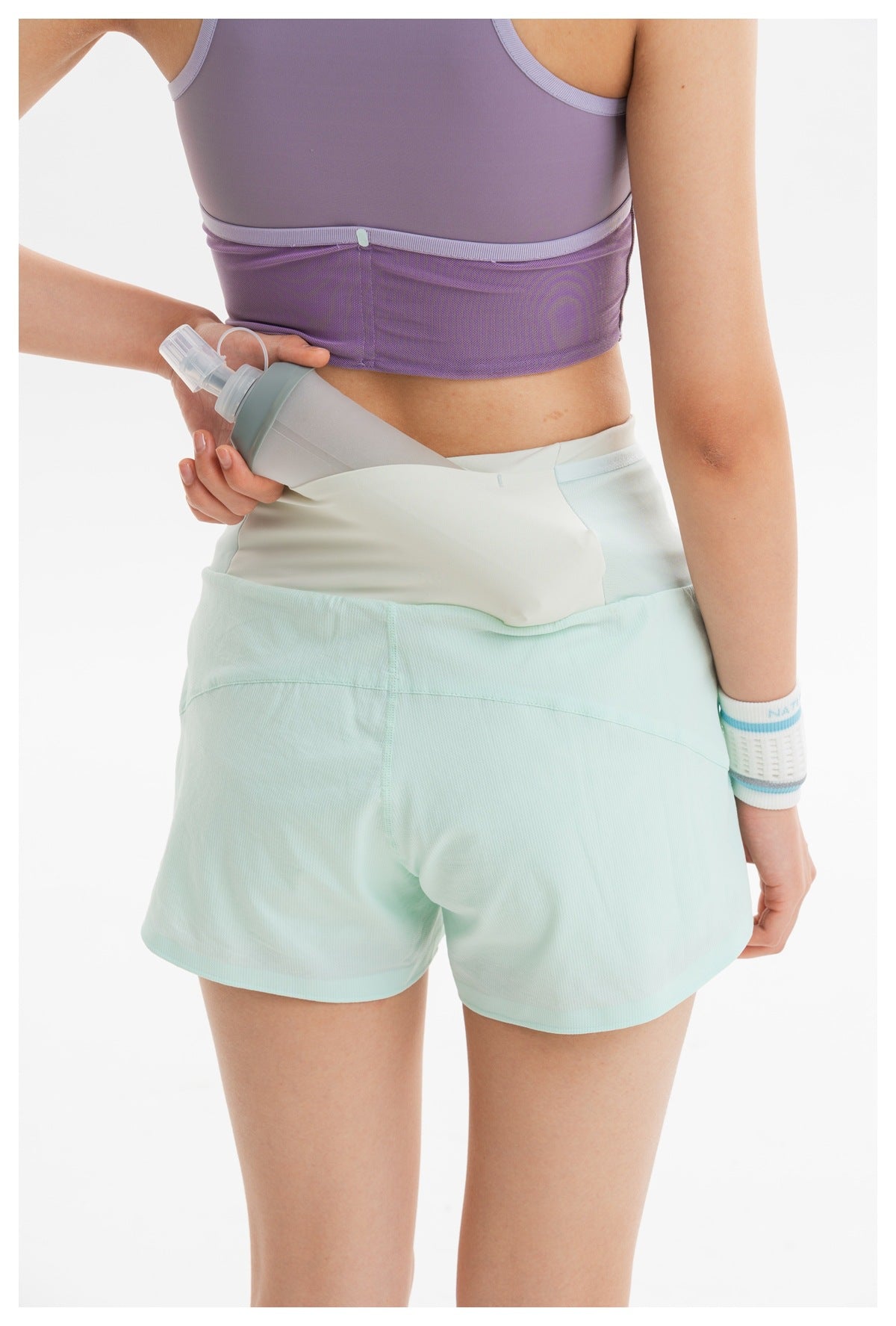 Close-up of a lavender sports bra and mint shorts, showing a waistband pocket holding a water bottle.