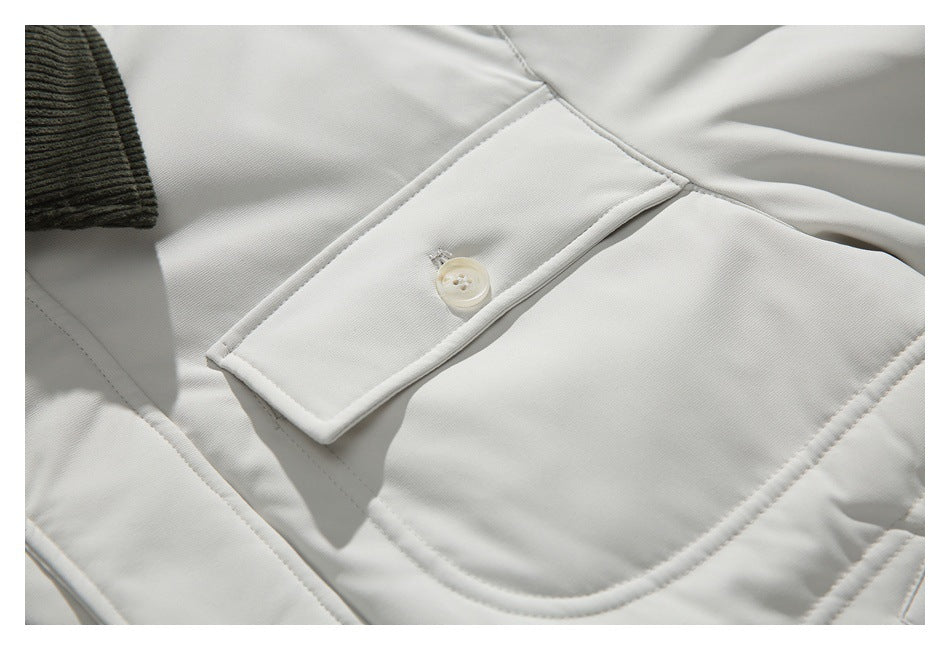 Close-up of an ivory jacket pocket flap with a button, curved stitching, and part of a dark ribbed collar.