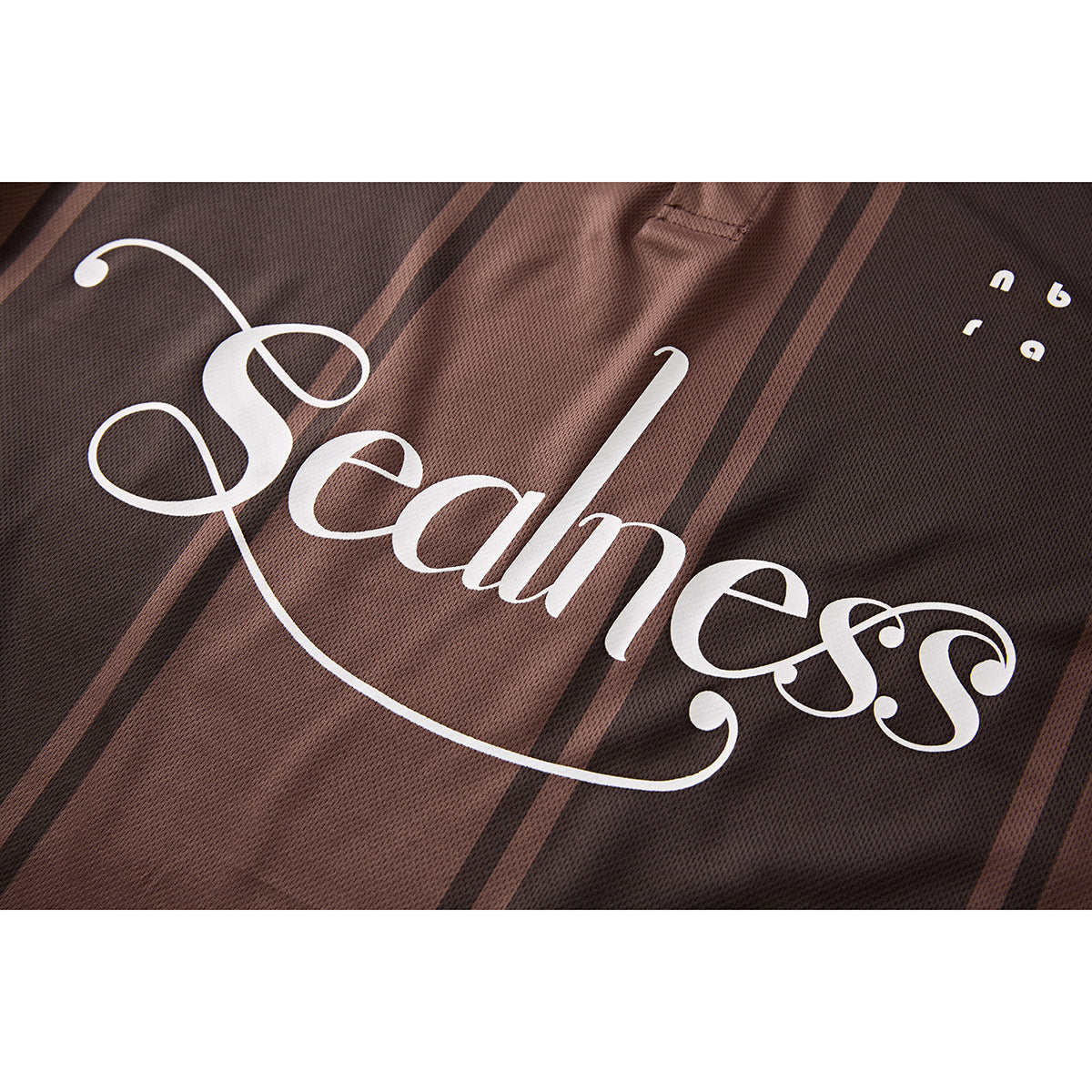 Close-up of ornate white “Seamless” lettering on the dark brown striped polo shirt.