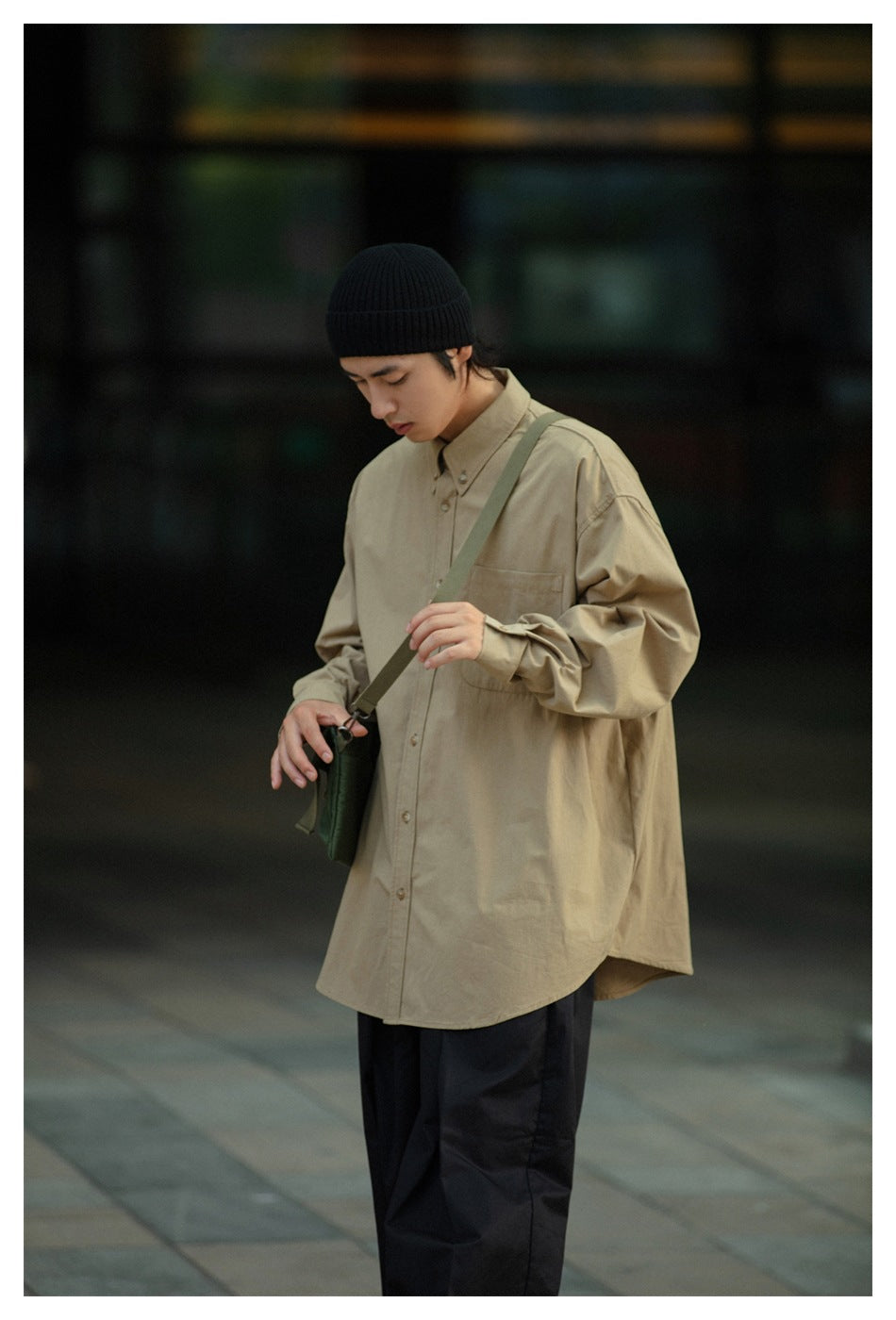 Closer view of a model in an oversized khaki button-up shirt, black trousers, and a green crossbody bag.