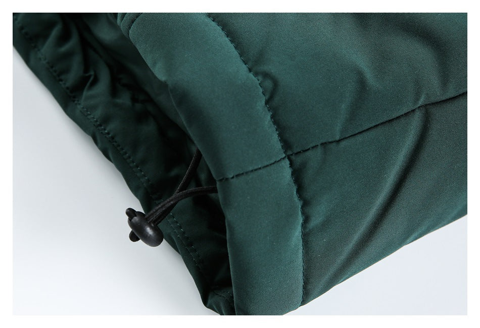 Close-up of dark green garment fabric with a black drawcord and toggle beside a stitched edge.