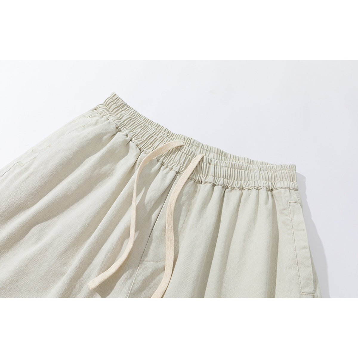Close-up of ivory pants showing the gathered elastic waistband, long drawstrings, and side pockets.
