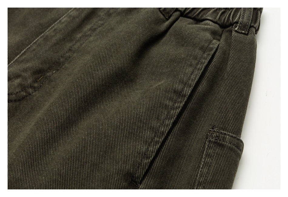 Close-up of dark olive trousers showing the elastic waistband, diagonal seams and edge of a side pocket.