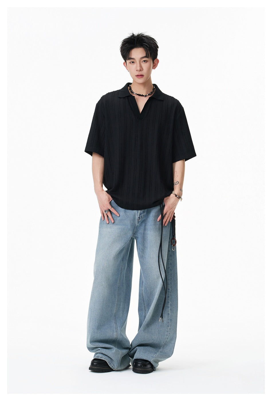 Front view of a model wearing a black short-sleeve polo with a collar and open placket, paired with wide light-blue jeans.