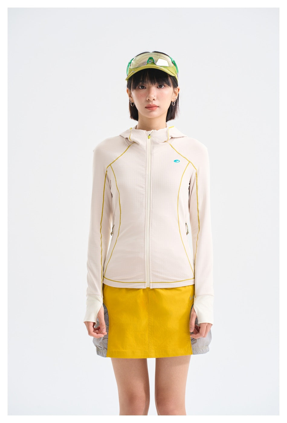 Front view of a model in an ivory hooded zip jacket with yellow piping and a yellow-and-gray skirt.