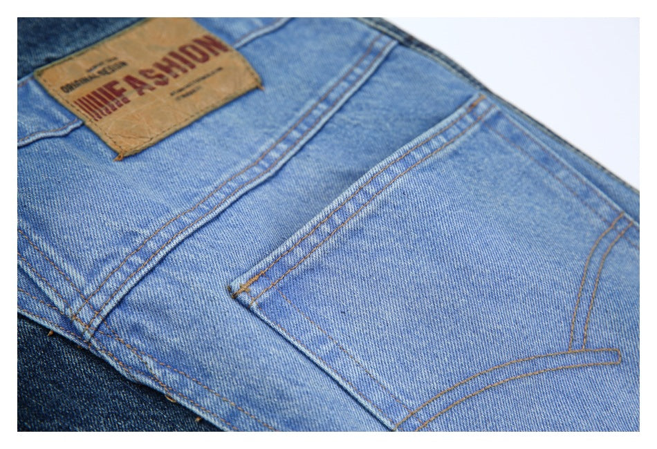 Close-up of light blue jeans showing a back pocket, contrast stitching, and a tan leather waistband patch with lettering.