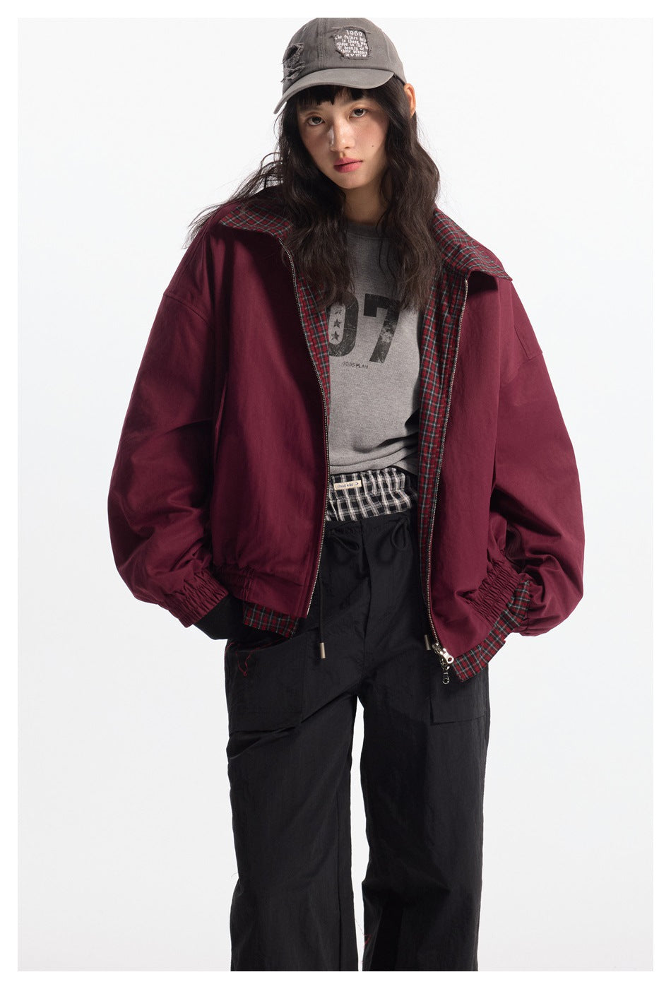 Model wearing an open burgundy jacket with red-and-green plaid lining and collar, paired with black pants.