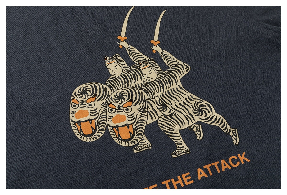 Close-up of a beige-and-orange graphic showing two figures riding tiger-faced forms on the charcoal shirt.