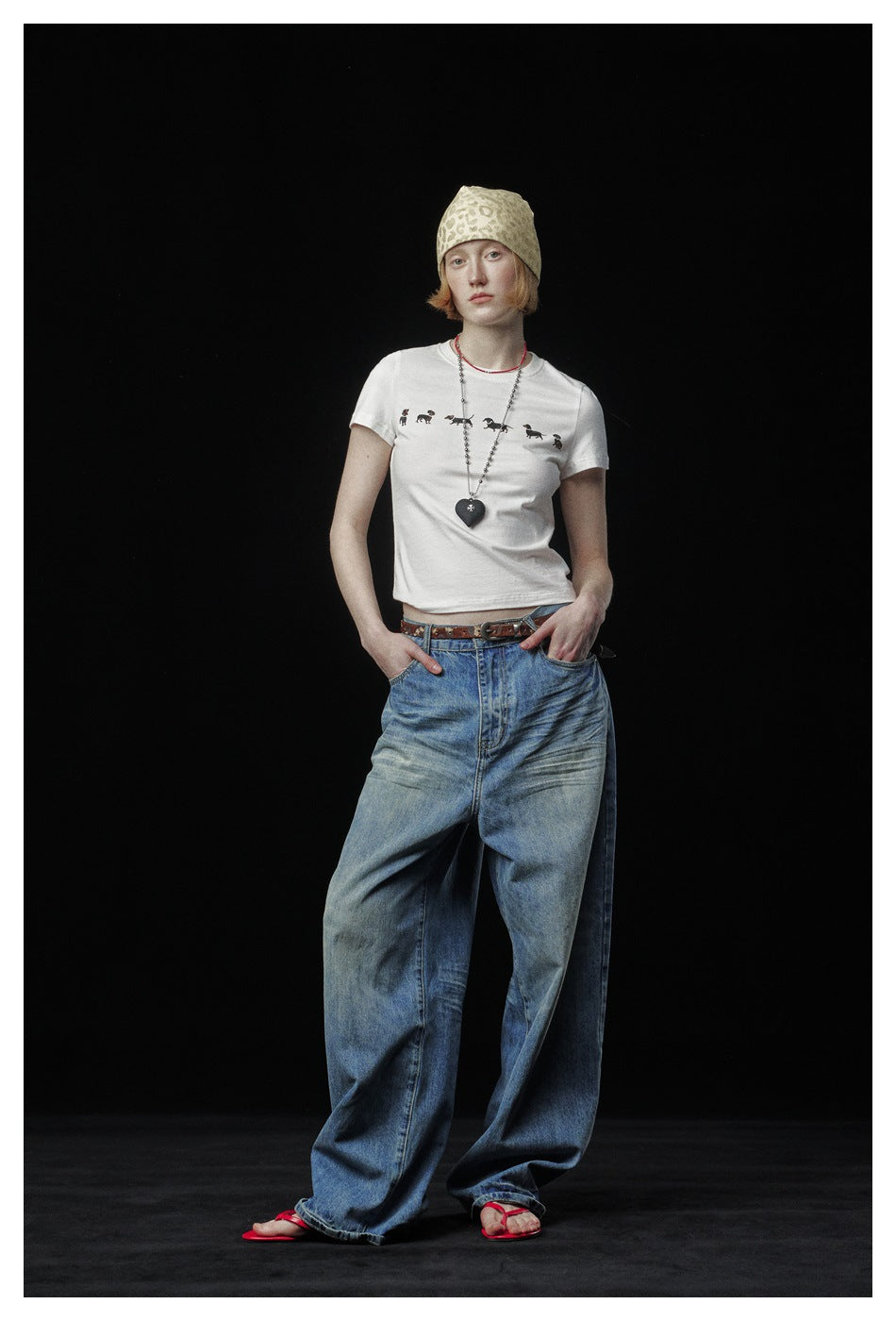 Model wearing a white dachshund-print T-shirt with wide-leg blue jeans, a patterned beanie and a heart pendant necklace