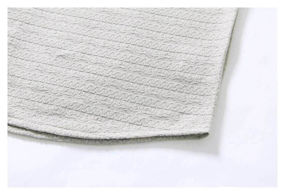 Close-up of the hem of a light gray shirt with a raised geometric stripe pattern.