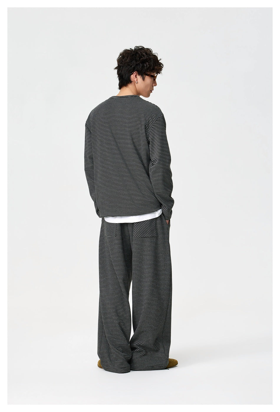Rear view of a model wearing a black thin-striped henley and matching loose trousers.