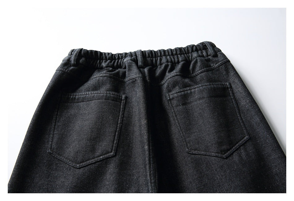 Back view of black textured trousers laid flat, showing a gathered waistband and two patch pockets.