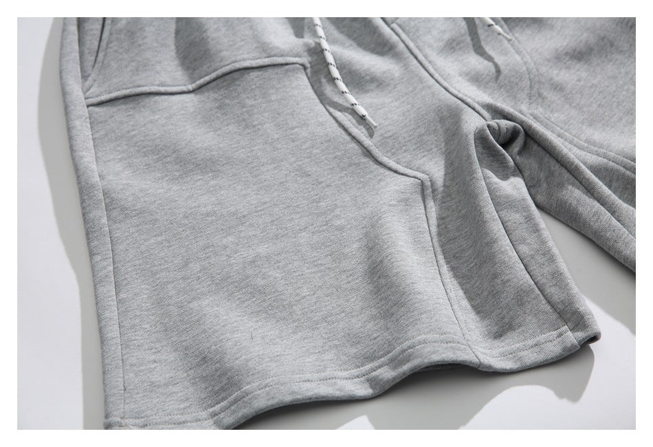 Close-up of gray sweatpants showing a front pocket, seams, and white drawstrings with black markings.