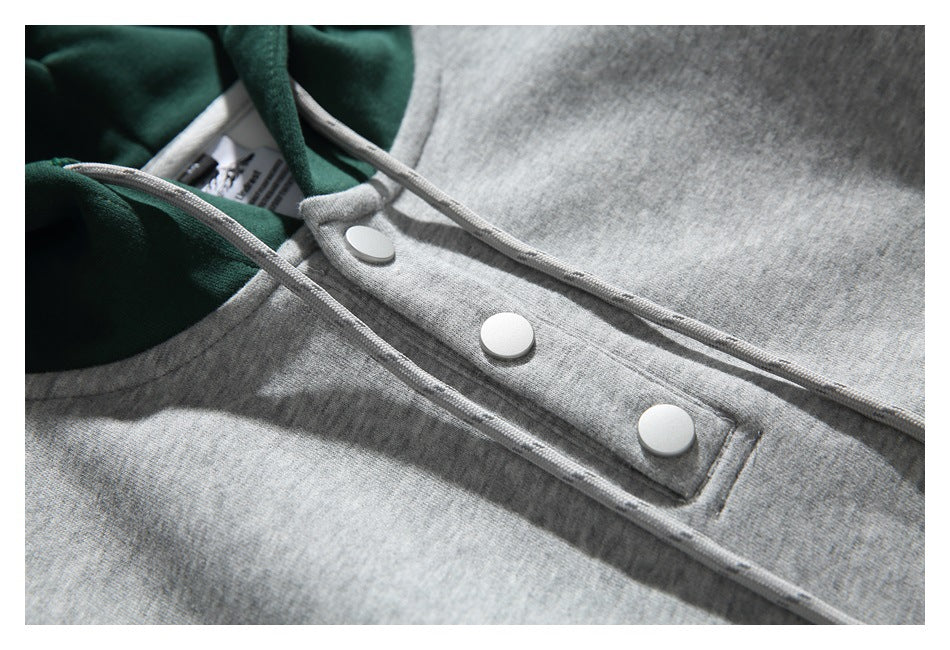 Close-up of the gray hoodie’s three white snaps, gray drawstrings, and dark green hood lining.
