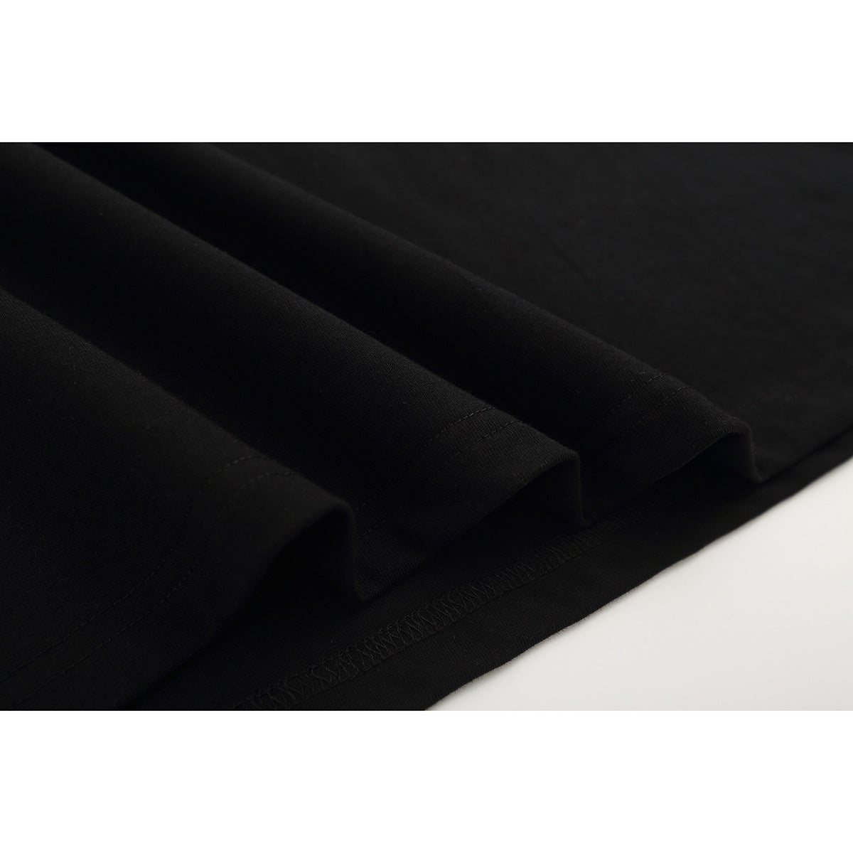 Close-up of black T-shirt fabric folds, stitched hems, and overlocked seam.
