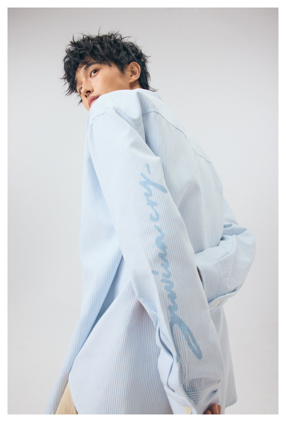 Model wearing a pale blue and white pinstriped shirt, showing its side and a large graphic on the sleeve.