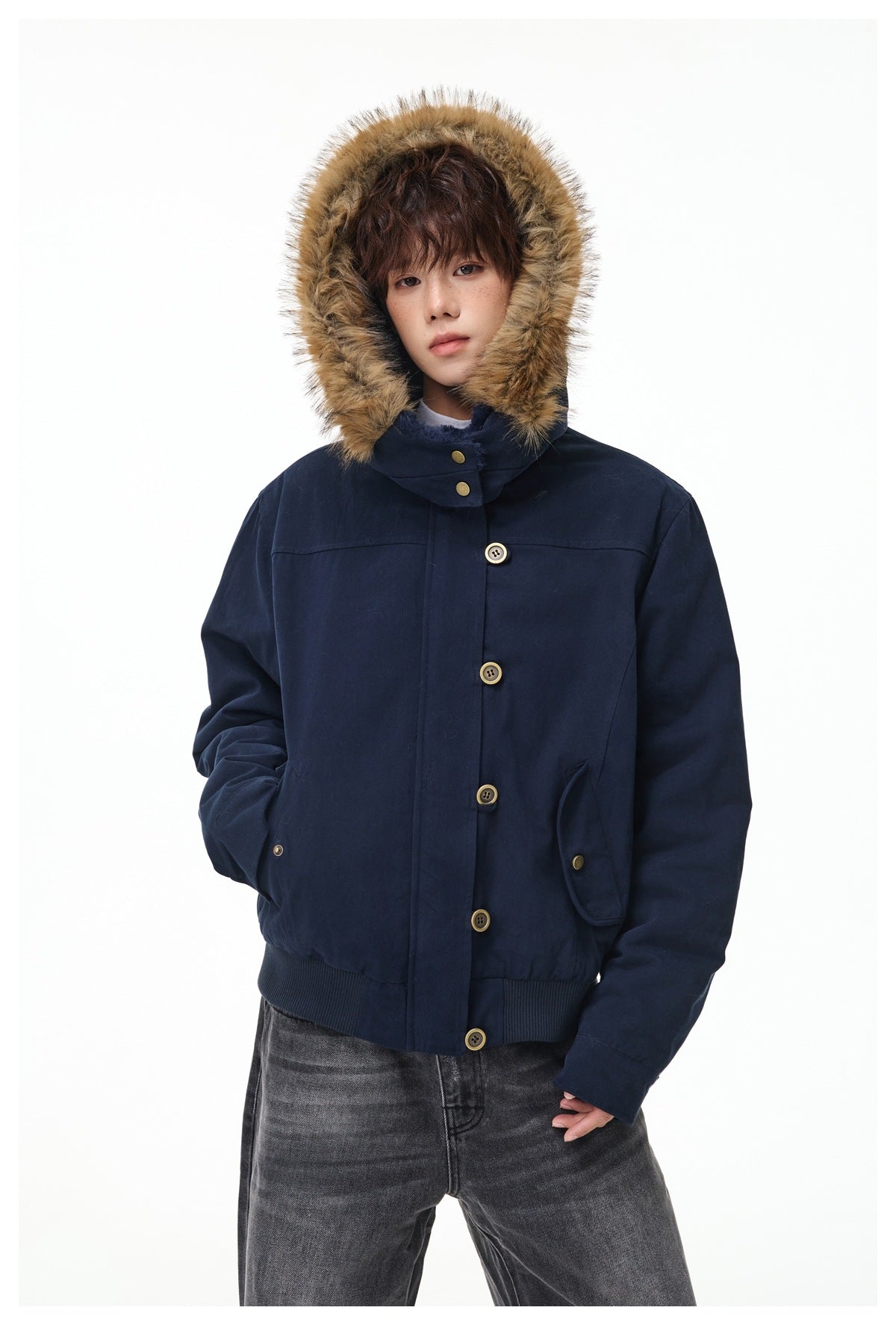 Person wearing a navy hooded jacket with faux-fur trim, buttoned up with the hood raised, paired with gray jeans